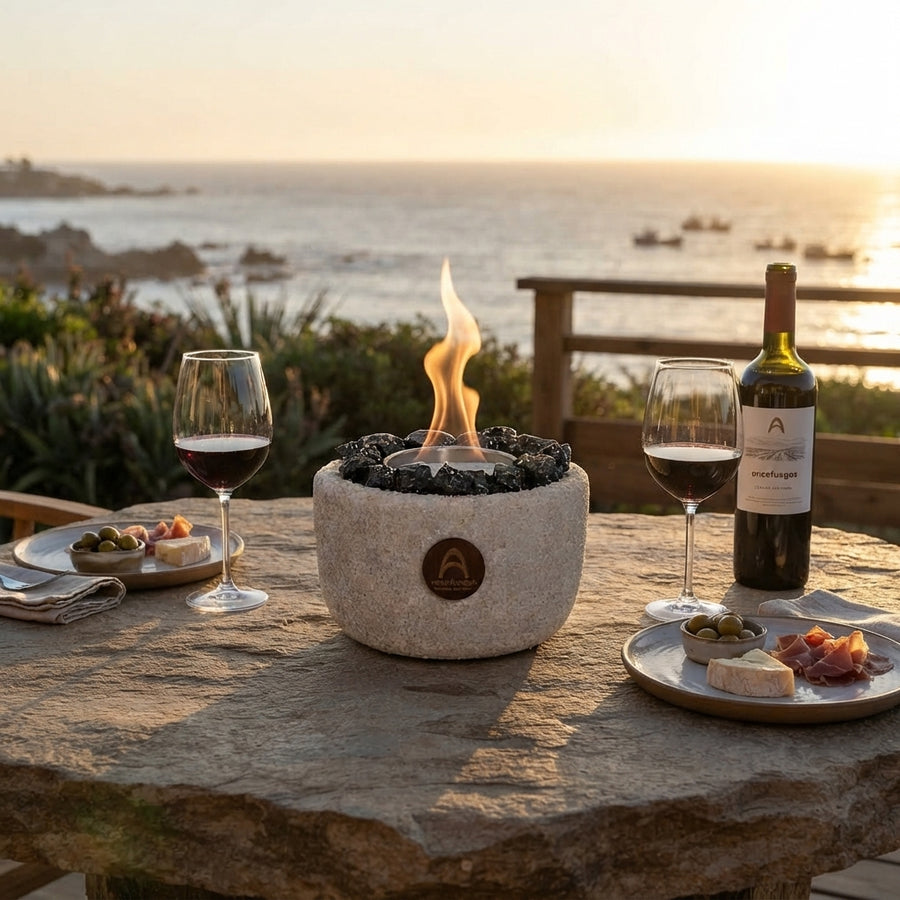 Elquí Compacto Obsidiana encendido en una mesa de piedra frente al mar, con copas y vino