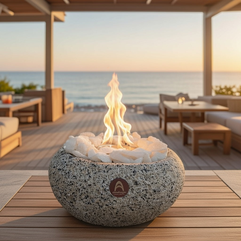 Fogón Costa Grande Arena Clara encendido con piedras blancas, en un deck de madera con vista al mar